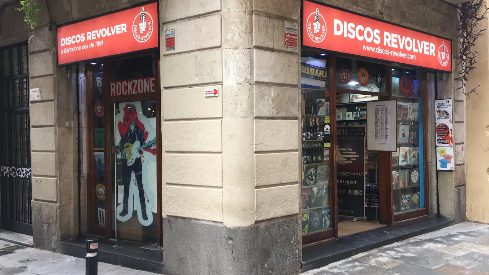 Storefront of Discos Revolver, a record shop in Barcelona, with red signage and vinyl sleeves in the window