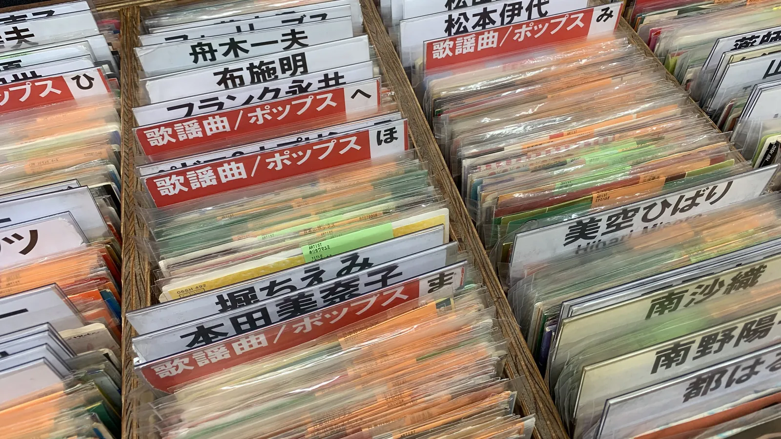 Cajones de discos japoneses de segunda mano en fundas de plástico, ordenados tras separadores rojos de kayōkyoku/pops y tarjetas con el nombre de cada artista, en una tienda de discos de Shinjuku, Tokio